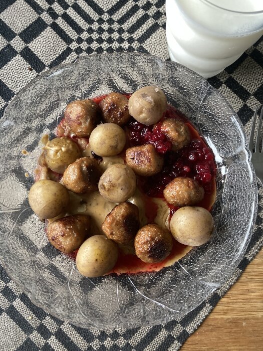 Köttbullar, potatis, lingonsylt, gräddsås på tallrik med rutigt underlägg, glas mjölk. Typisk svensk måltid.