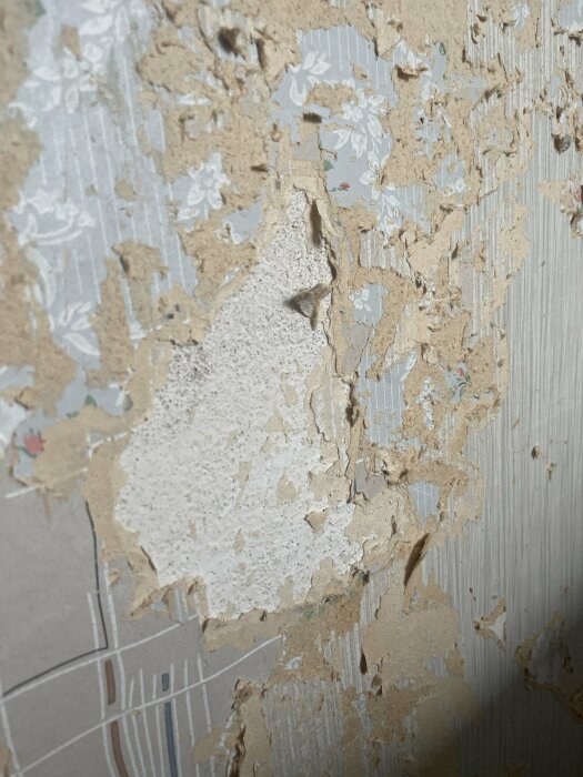 Flera lager flagnande tapet och färg på en vägg. Renovering eller skada synlig.