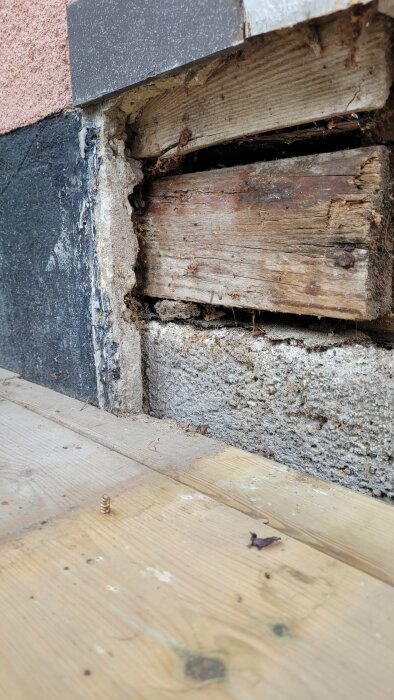 Skadat trä och betongvägg med synlig isolering, behöver renovering.