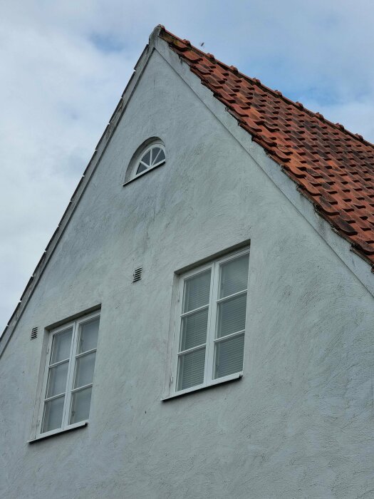 Gavel på hus med vita väggar, röda takpannor, fönster och dekorativt kvistfönster.