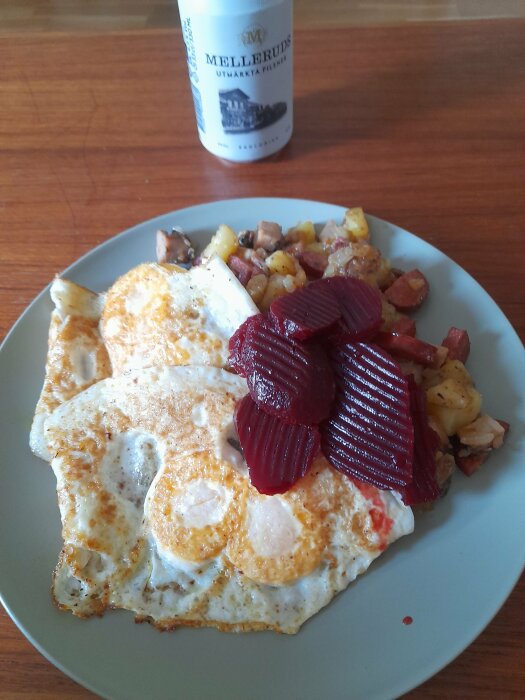 Stekt ägg, rödbetor, potatis, tärnat kött, Melleruds ölflaska, träbord.