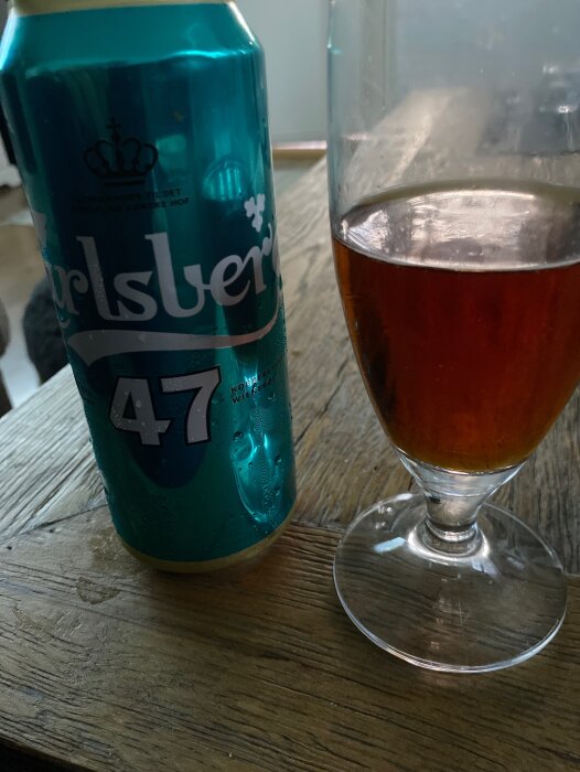 En Carlsberg ölburk bredvid ett ölglas halvfyllt med bärnstensfärgad dryck på ett träbord.