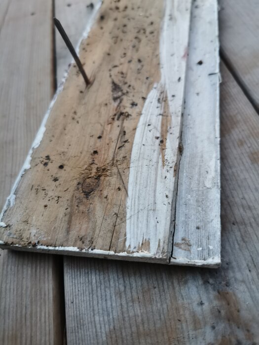 Närbild på vitmålat, slitet trä med en rostig spik. Texturen visar ålder och väderexponering.