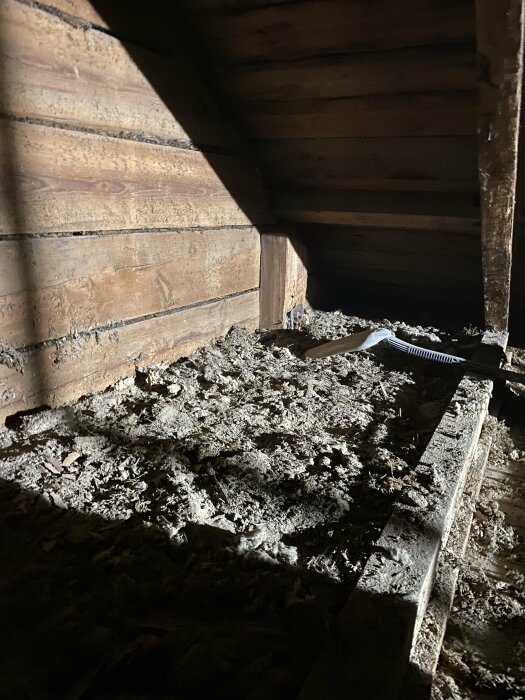 Mörkt vindutrymme, träväggar, spillror på golvet, skuggor och ljusstrimma, övergivet intryck.