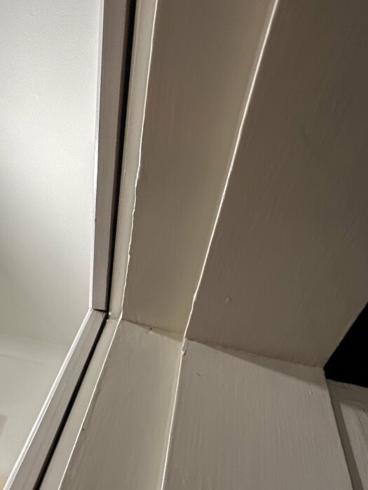 Vit målad dörrkarm och vägg, närbild. Vertikala och horisontella linjer möts. Inomhusbelysning. Minimalistisk. Enkelhet.