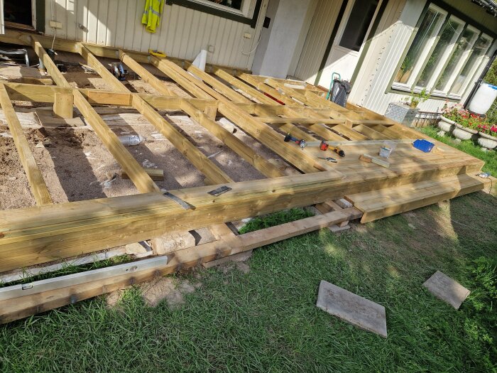 Trädäck under konstruktion vid ett hus, verktyg och byggmaterial synligt.