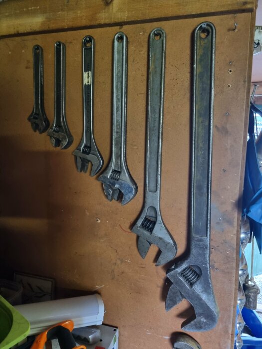 Fem upphängda skiftnycklar i olika storlekar på en trävägg i en verkstad.