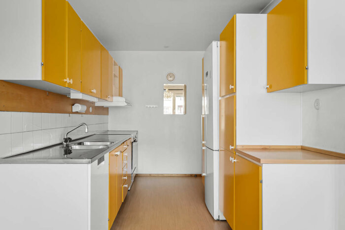 Ett kök med vita väggar, gula skåp, träbänkar, och rostfri diskbänk.