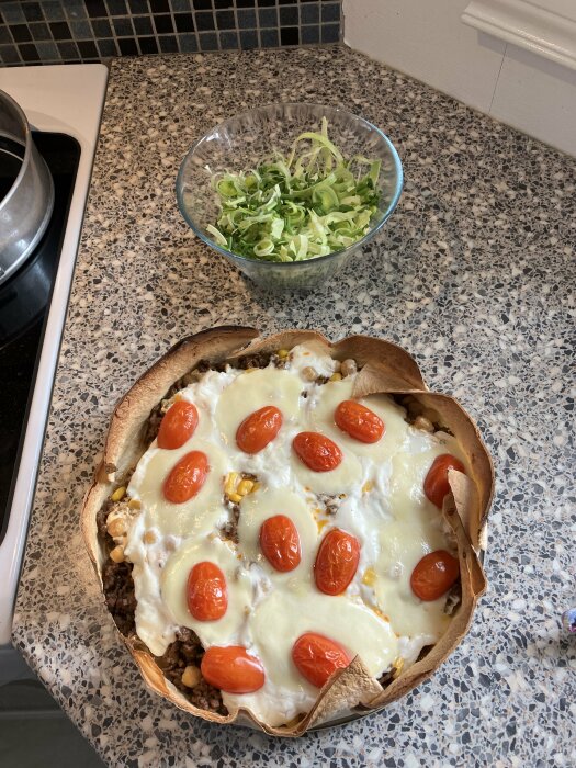 Hemlagad pizza med tomater och ost, salladskål bredvid, på köksbänk.