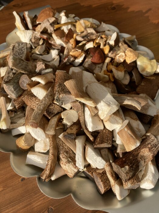 Tallrik med torkade svampar på ett träbord, varierade färger och former, naturligt ljus.