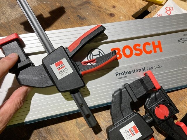 Bosch-skena och Bessey-klämmor på träbord, verktyg för snickeri eller träbearbetning, hand som håller klämma.