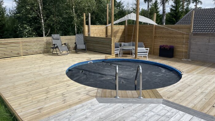 Utomhus träterrass med halvtäckt rund pool, uteplatsmöbler, solstolar, plantering och parasoll.