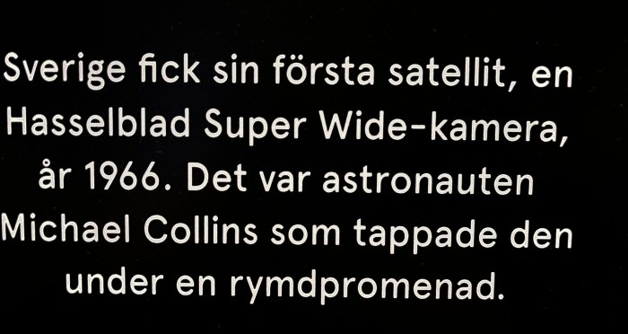 Text om Sveriges första satellit, Hasselbladskamera, tappad av astronauten Michael Collins 1966. Svart bakgrund, vit text.