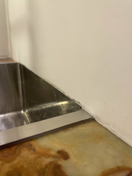 Hörn av ett kök med rostfri diskbänk, smutsig kakelskiva och vit vägg.