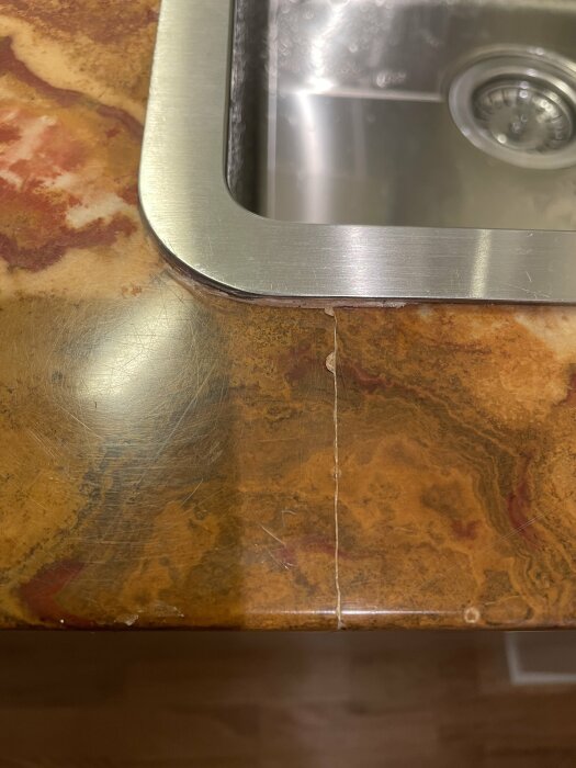Närbild på ett kökshörn med rostfritt stål diskho och bänkskiva med marmormönster.