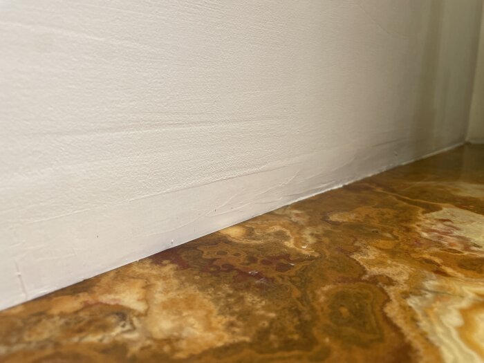 Väggmöte golv med vit list och mönstrat brunt golv. Skarpa hörn, interiördetalj, närbild.