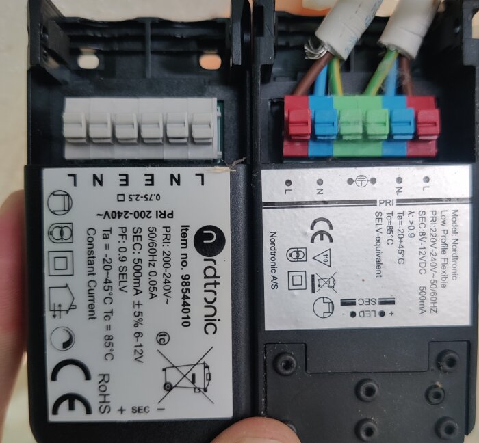 Elektronisk apparat, troligen strömförsörjningsenhet, med kablar och kontakt, etiketter med tekniska specifikationer.