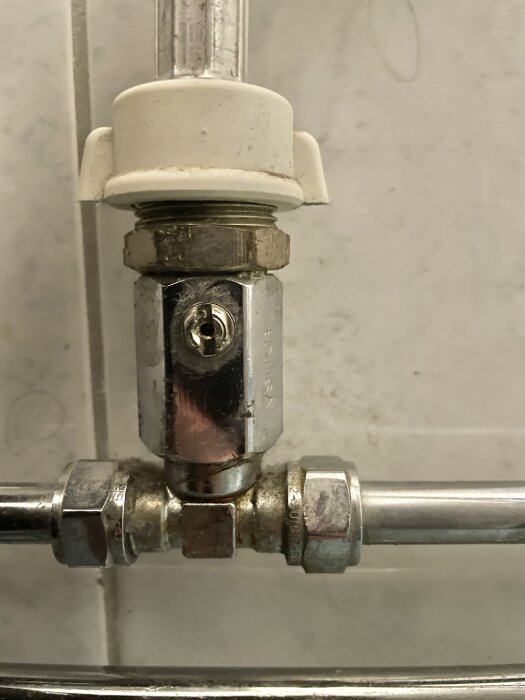 Rörkoppling och ventil med säkerhetslås på vit bakgrund, förmodligen i en dusch eller badrum.