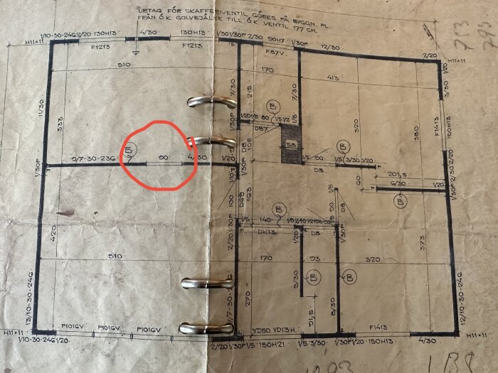 Gammal arkitektritning med måttangivelser, cirkelmarkerat område, metallklämmor och slitage.