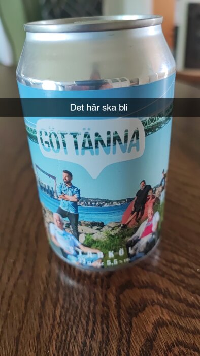 Ölburk med landskap, människor, text "GÖTTÄNNA", vattenutsikt, klippor, 5,5% alkohol, delvis synlig hand.