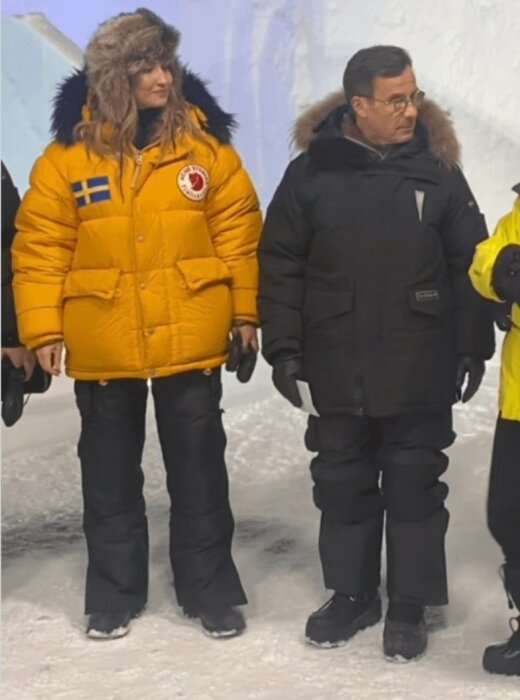 Två personer i tjocka vinterjackor, en med svenska flaggan, står i en kall, isig miljö.