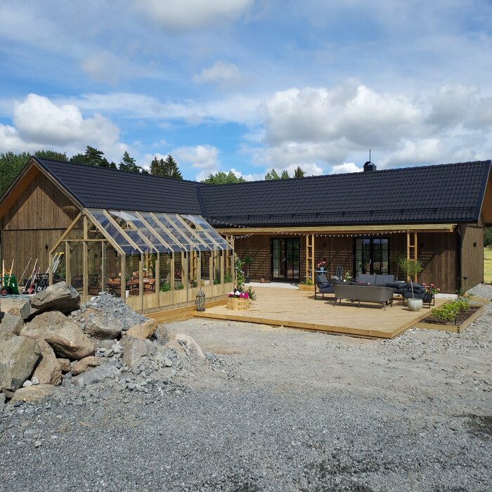 Trähus med terrass och växthus, molnig himmel, ingen synlig person, landskap under utveckling och konstruktion.