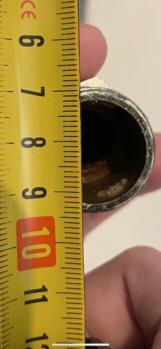 Mätband bredvid ett rör; skala visar cirka 8 centimeter; arbetsmiljö; mätning pågår.