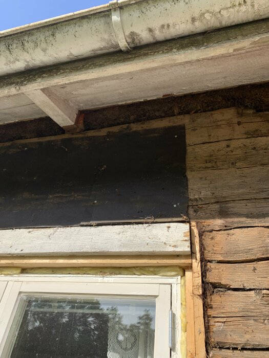 Hustak med synlig skada, fukt eller röta, behöver reparation, med hängränna, fönster nedanför.