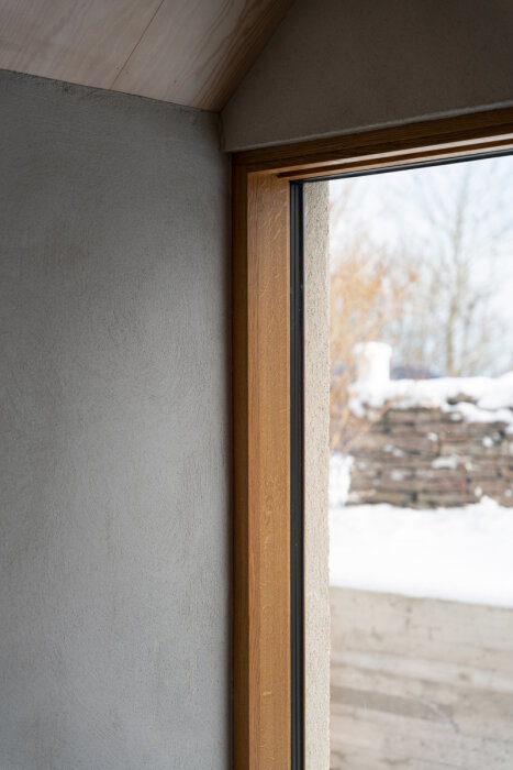 Hörn av ett rum med fönster, trädetaljer, utsikt över snötäckt landskap.