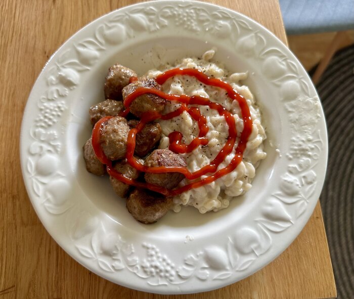 Ett fat med köttbullar och makaroner toppade med ketchup på ett träbord.