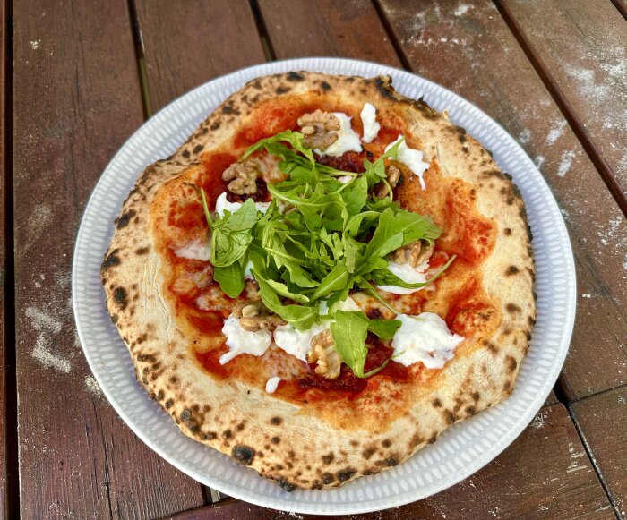 Pizza med tomat, mozzarella, valnötter, rucola på snöig träbord.