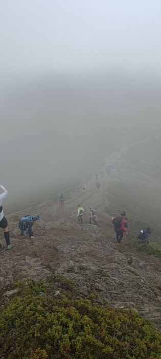 Vandrare i dimma klättrar bergsstig; säkerheten kan vara utmanande i dålig sikt. Natur, utomhusaktivitet, äventyr.