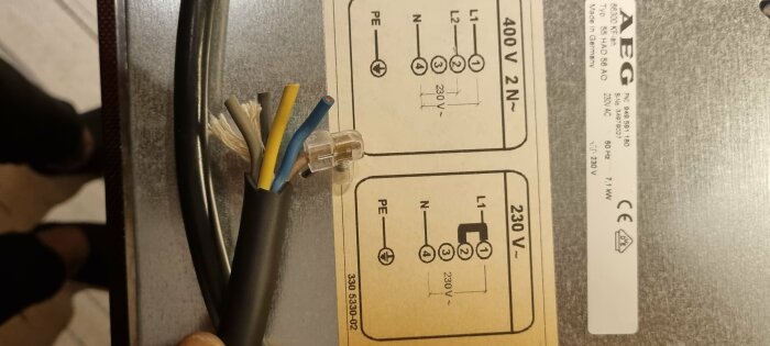 Elkabel avskalad framför kopplingsschema på vit etikett, AEG-märkt, 400V och 230V anvisningar.