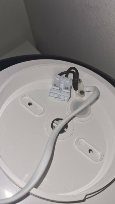 En vit lampsockel med elektriska anslutningar, skruvar, och en vit kabel.