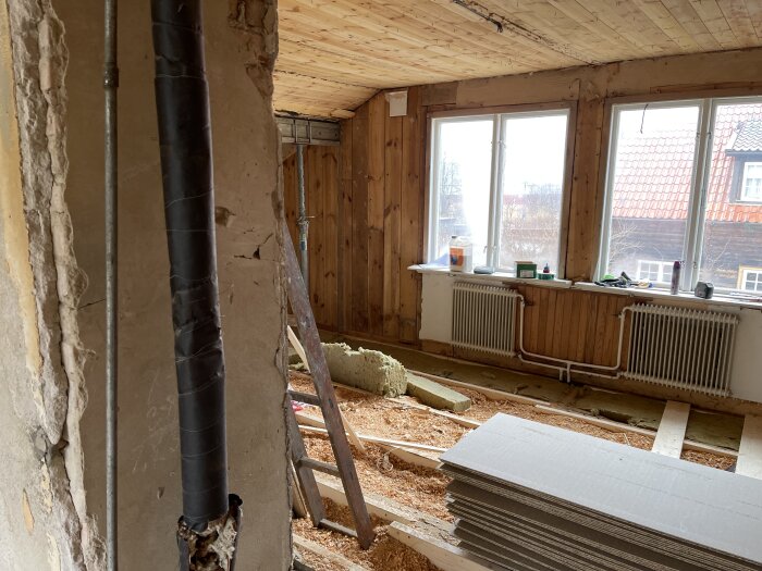 Renoveringsarbete pågår i ett tomt rum med isolering, byggmaterial, och exponerade träbjälkar.