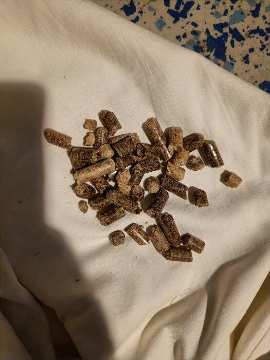 Trähärdade pellets och en metallmutter på vit tygduk, kanske för biobränsleanvändning eller djurströ.