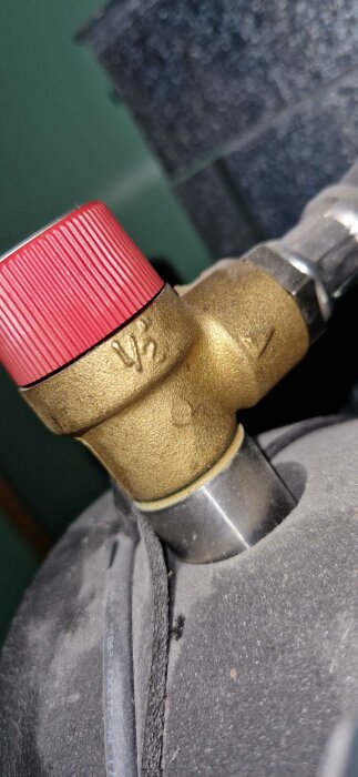 Röd ventilkåpa på en mässingsventil, ansluten till ett rör eller maskindel, möjligtvis VVS-relaterat.