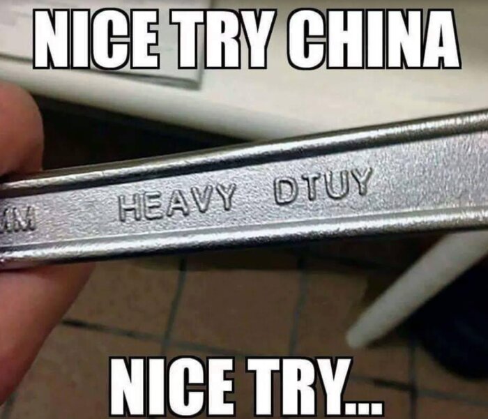 Handhållna tänger med stavfel "HEAVY DTUY" och ironiska textöverlägg "NICE TRY CHINA." Humorbild om produktionsmiss.