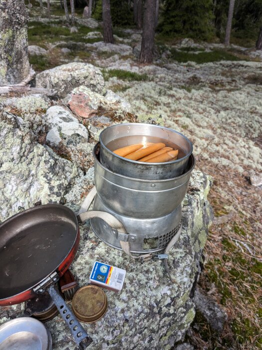 Friluftskök med kokta korvar i kastrull, stekpanna, tändstickor, i skogsmiljö.
