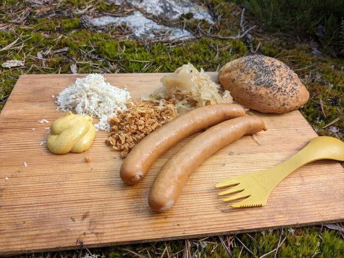 Utomhus måltid med korv, surkål, bröd, senap, rostad lök, spork. Träskärbräda på mossig mark.