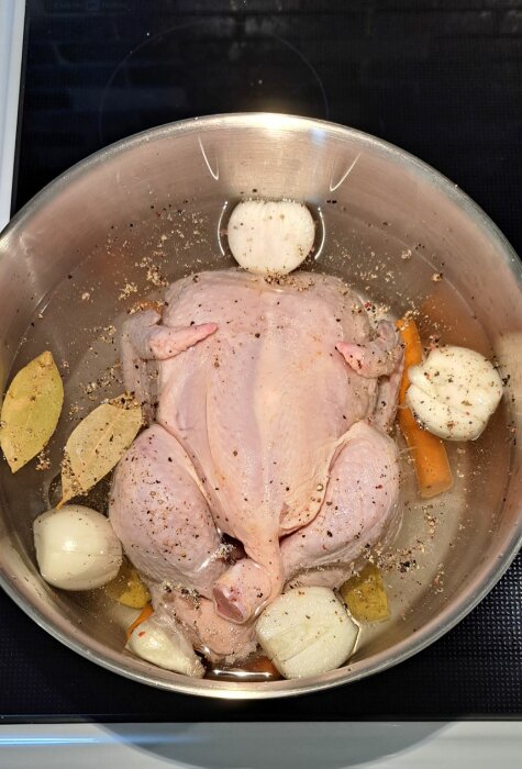 En rå kyckling med kryddor, morötter och lök i en matlagningspanna, förberedd för tillagning.