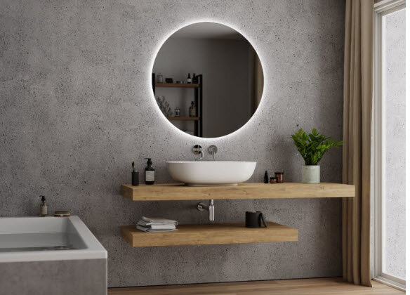 Modernt badrum med rund spegel, trähyllor, handfat, växter och gråa väggar.