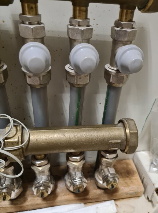 Rörkopplingar, ventiler och slangar, troligen en del av VVS-installation, på ett brunt träunderlag.