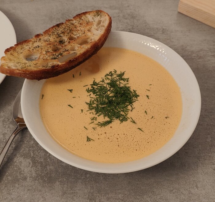 Krämig soppa med dill, rostat bröd på tallrik, grått bord.