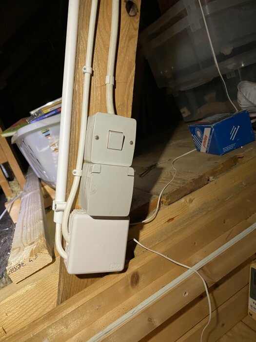 Elektrisk installation med strömbrytare och dosa på träbjälkar, taklampans förpackning, suddig bakgrund av förrådsartiklar.