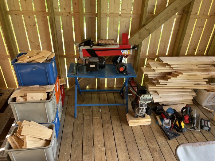 Träarbetsområde med såg, träplank, verktyg och förvaringslådor i halvfärdig träkonstruktion.