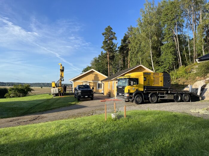 Byggarbetsplats med grävmaskin, lastbil och byggnader under klar himmel.