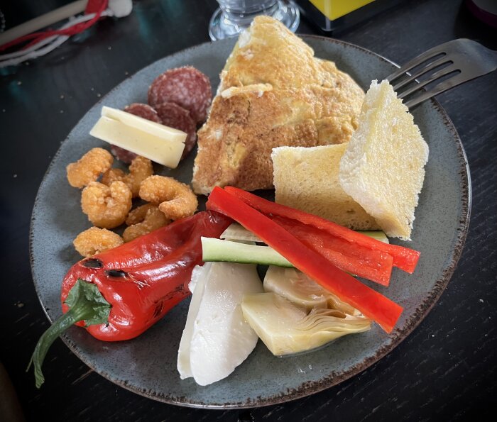 Färgglad tallrik med omelett, salami, ost, knapriga snacks, rostad paprika, gurkstavar, konserverad kronärtskocka och vitt bröd.