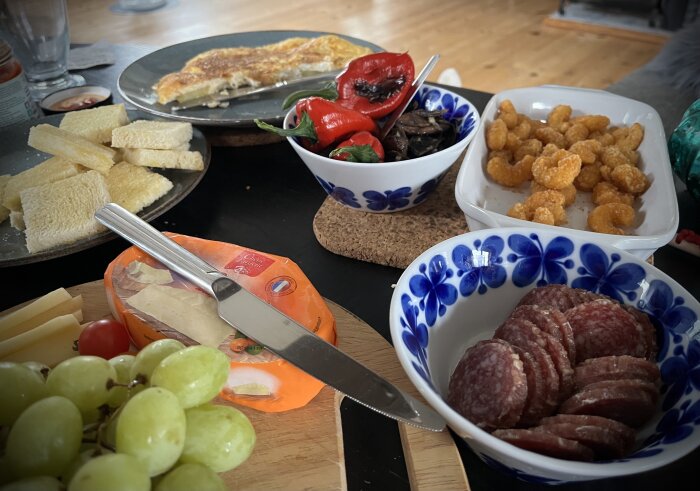 Matbord med ost, salami, druvor, paj, rostat bröd, och inlagda grönsaker.