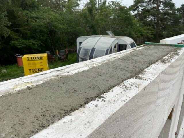 Färsk betong på en mur, med gröna träd och en husvagn i bakgrunden. Byggarbetsplatsens stämning.